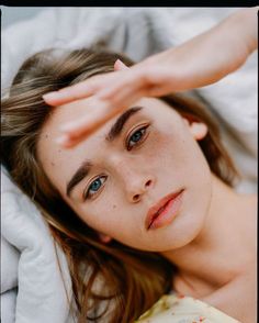 a woman laying on top of a bed with her hand over her head and looking at the camera