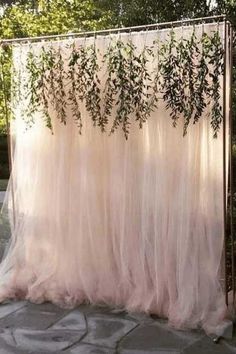 an outdoor wedding ceremony with pink tulle and greenery draped over the back wall