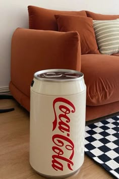 a coca - cola can sitting on the floor in front of a couch with pillows