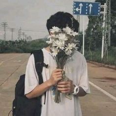 a person with flowers in their face standing on the side of an empty road next to a street sign