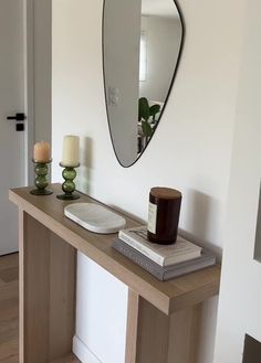 a mirror on the wall above a table with books and candles in front of it