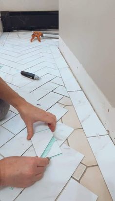 a man laying tile on the floor with his hands pointing at it while he is working