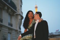 a man and woman standing next to each other in front of a building at dusk