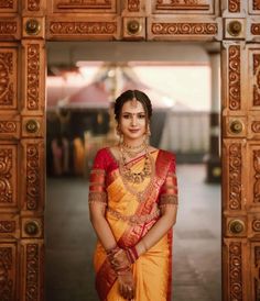 a woman in an orange and yellow sari standing by a wooden door with her hands on her hips