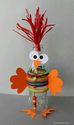 a bird made out of paper sitting on top of a jar filled with yarn and feathers