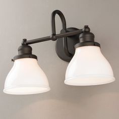 two light bathroom fixture with white glass shades on the top and dark metal arm, against a gray wall