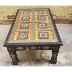 a coffee table with an intricate design on the top and bottom, sitting in front of a stone wall