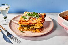 a plate with lasagna on it next to a glass of water and utensils