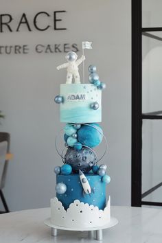 a three tiered cake decorated with blue and silver decorations on top of a white table