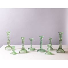 a group of green glass candlesticks sitting on top of a white table next to each other