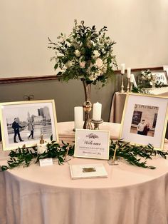 a table topped with pictures and flowers on top of a white cloth covered round table