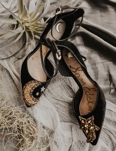 two pairs of black shoes with gold sequins on them sitting next to a flower