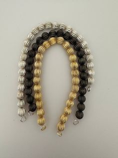 three strands of black, silver and gold bracelets on a white surface with one bead in the middle