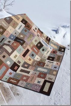 a quilted blanket sitting on top of a snow covered ground next to a tree