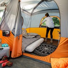 a woman standing in the doorway of a tent with an open door and bed inside