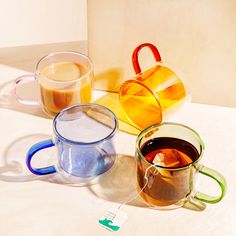 three different colored coffee mugs sitting next to each other on a white counter top