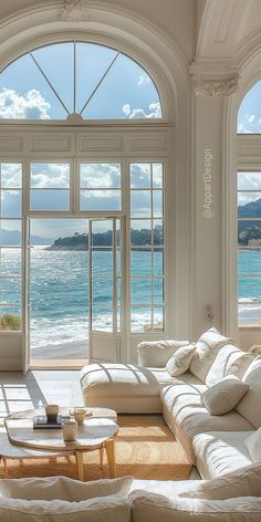 a living room filled with white furniture and large windows overlooking the ocean on a sunny day