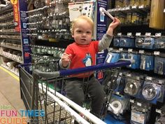 a young boy sitting in a shopping cart holding up a cell phone and pointing at it