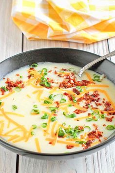 a bowl of soup with cheese, bacon and green onions on the table next to a napkin