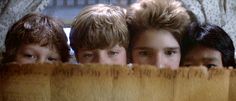 three young boys looking over a wooden slatted fence with their faces peeking through the slats