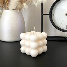 a white vase filled with lots of flowers next to a clock and some dried plants