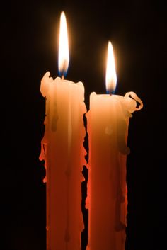 two lit candles are shown in the dark