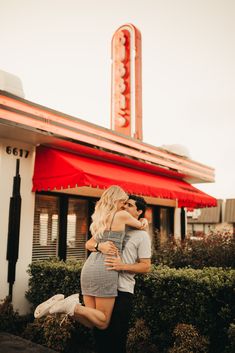 a man and woman hugging in front of a building with a neon sign on it