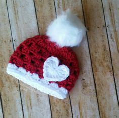 a red and white knitted hat with a heart on the front sitting on a wooden floor