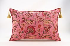 a pink and gold pillow with tassels on the ends, sitting on a white surface