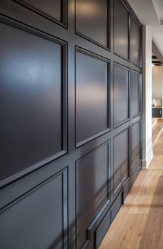 an empty hallway with wood floors and black paneling on the wall, leading to another room