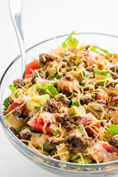 a salad with meat, cheese and tomatoes in a glass bowl