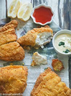 fried fish with dipping sauce and lemon wedges on newspaper next to small bowl of ketchup