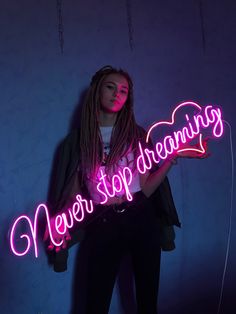 a woman holding a neon sign that says never stop dreaming