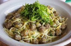 a white bowl filled with pasta and meatballs on top of a table next to a fork