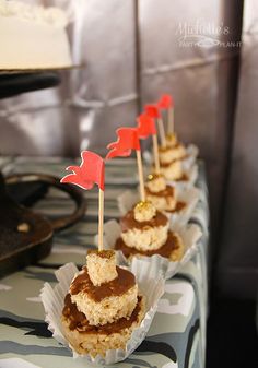 small cupcakes are lined up on a striped tablecloth with red flags sticking out of them