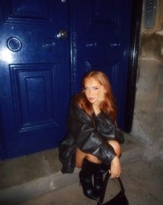 a woman sitting on the ground in front of a blue door holding a black purse