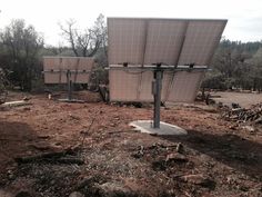 three solar panels sitting on top of a dirt covered field with trees in the background