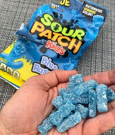 a hand holding blue raspberries next to a bag of gummy pees