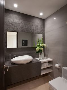 a white sink sitting on top of a counter next to a toilet and a vase with flowers in it