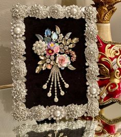 an ornate frame with pearls and flowers in it on a table next to other decorative items