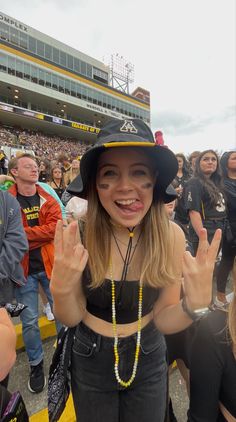 a woman wearing a black hat and holding her hands up in the air at a football game