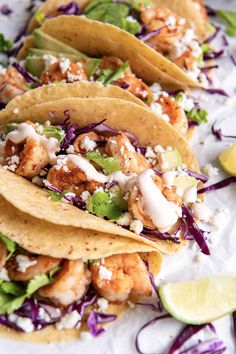 three tacos with shrimp, lettuce and shredded cheese on top are sitting on a white plate