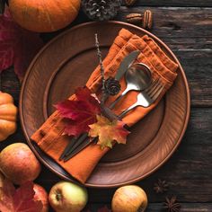 an autumn place setting with orange napkins, silverware and apples on a wooden table