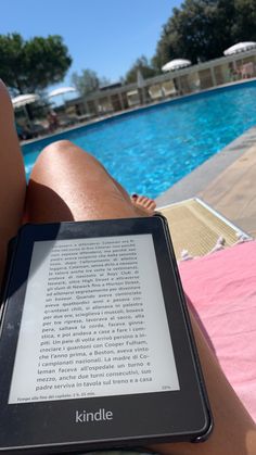 a person is sitting next to a swimming pool with a kindle on their lap