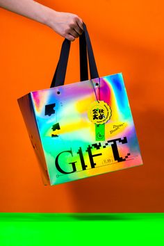 a person holding a colorful shopping bag in front of an orange wall with the word gift on it