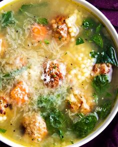 a bowl of soup with meatballs and spinach in it on a purple cloth