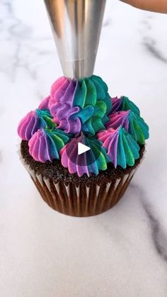 someone is decorating a cupcake with colorful icing