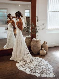 a woman standing in front of a mirror wearing a wedding dress and looking at her reflection