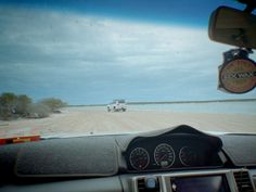 the dashboard of a car driving down a dirt road next to an open field and ocean