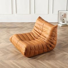 a brown leather chair sitting on top of a hard wood floor next to a white wall